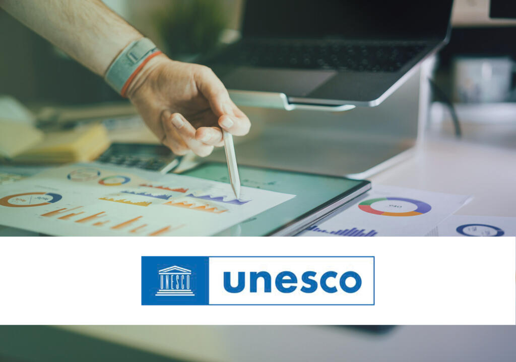 A person is holding a pencil and pointing at a graph. In the background, you see a laptop, a calculator and a tablet, representing an office setting. A white banner with the logo of UNESCO is placed over the image. The image represents a policy monitory article about a UNESCO document. 

Een persoon houdt een potlood vast en wijst naar een grafiek. Op de achtergrond zie je een laptop, een rekenmachine en een tablet, die een kantooromgeving voorstellen. Een witte banner met het logo van UNESCO is over de afbeelding geplaatst. De afbeelding stelt een beleidsartikel voor over een UNESCO-document.
