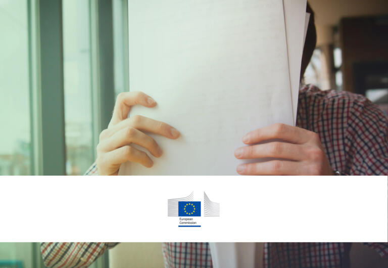 Person holding a pile of papers. There is a white banner with the logo of the European Commission. This show that this policy monitor item is about the European Commission