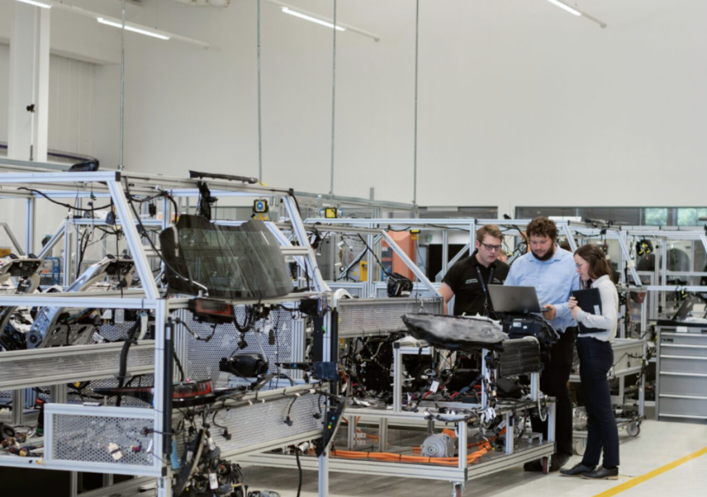 Three people stand next to industrial machinery in a bright, modern manufacturing facility, reviewing documents or data on a device.

Drie mensen staan naast industriële machines in een lichte, moderne productiefaciliteit en bekijken documenten of gegevens op een apparaat.