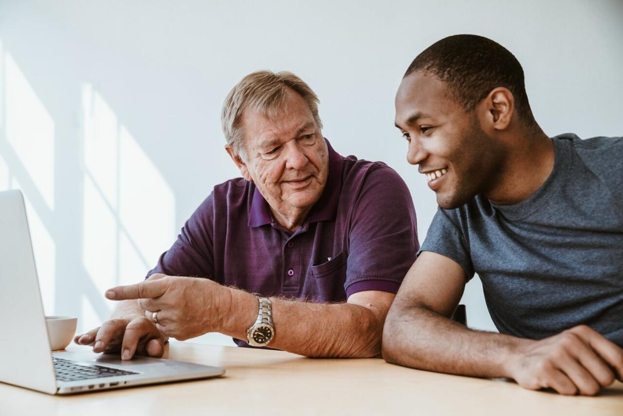 A man is showing another man something on a laptop screen