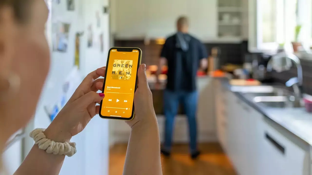 Woman playing something on her phone in a kitchen. A man is preparing something in the background.