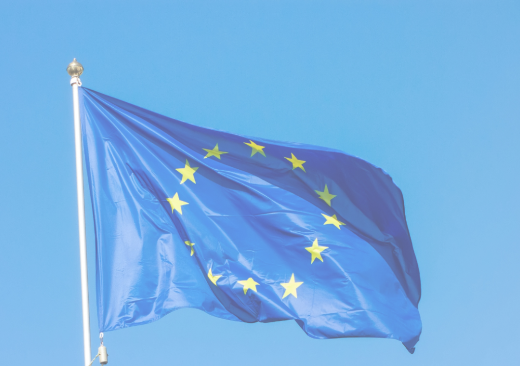 Vlag en wimpel van de Europese Unie (donkerblauw met gele sterren in een cirkel) tegen een blauwe lucht. 
Flag and pole of the EU (blue and yellow stars in a circle against the background of the blue sky.