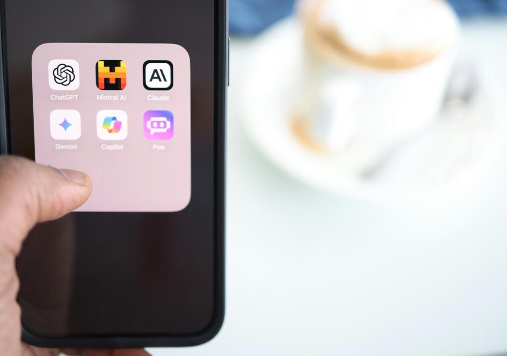 person holding a mobile phone. The screen shows several AI-chatbot applications, such as Mistral AI, Claude, Copilot and ChatGPT