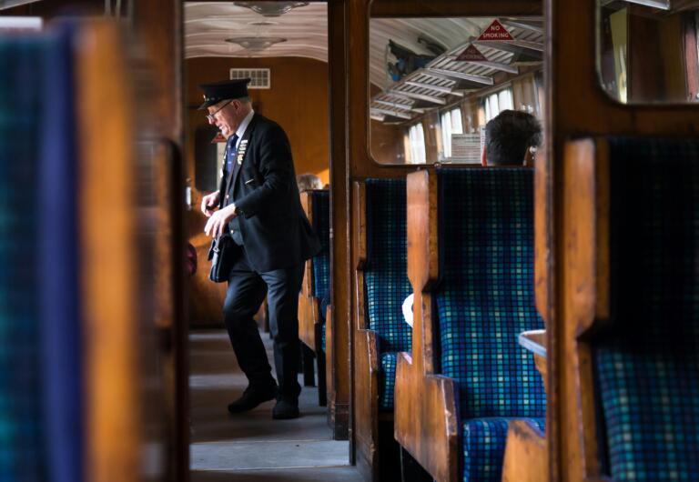 man-in-black-suit-standing-beside-brown-wooden-wall-train-conductor