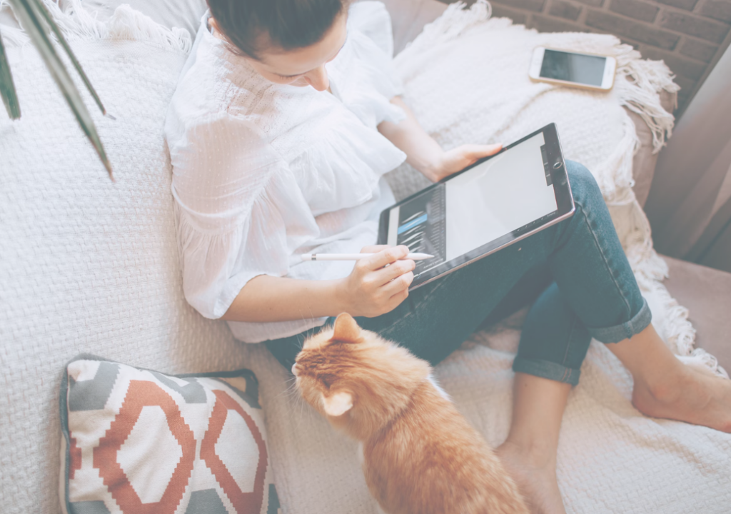 A woman sits on a couch with a cat beside her, focused on a tablet in her hand.
Een vrouw zit in de zetel met een kat naast haar, ze is gefocust bezig op haar tablet.