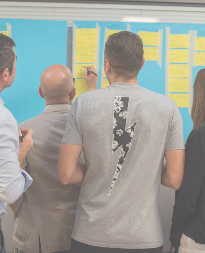 A diverse group of people gathered around a board covered in colorful sticky notes, engaged in discussion.
Een diverse groep mensen zijn verzameld rondom een bord met gekleurde sticky notes